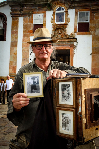 Fotógrafo Daniel em Tiradentes com sua máquina fotográfica e fotos em quadros - Foto: Danielli Queiroz