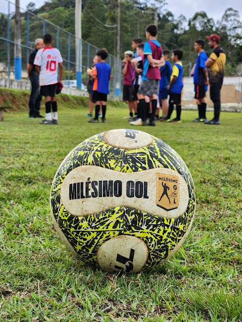 Bola parada na frente e turma tendo aula ao fundo.