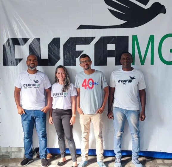 Integrantes da CUFA MG posam para foto na frente de um painel do programa.